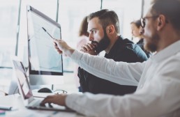 Man pointing something on his computer to his colleague